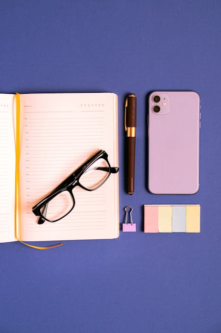 Elegant flat lay showcasing a notebook, eyeglasses, smartphone, pen, and sticky notes on a blue background.